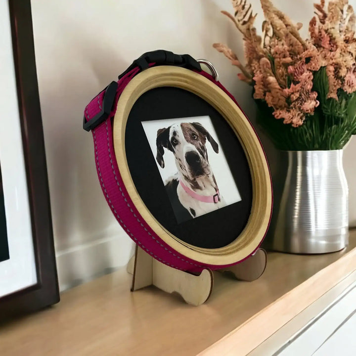 Great Dane memorial frame with pink collar and light wood border, displayed on a mantel beside artwork and dried flowers.