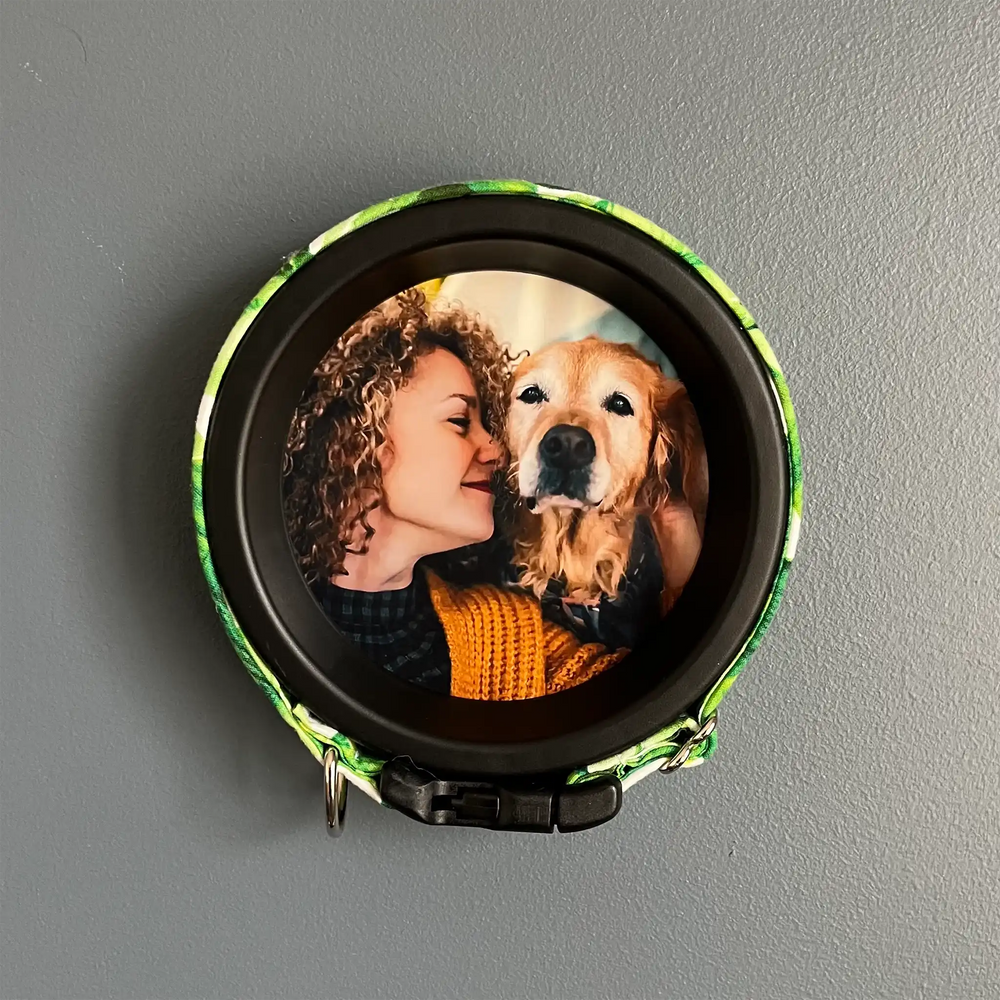 Dog memorial frame with colorful green floral collar displaying a photo of woman and senior Golden Retriever on gray wall