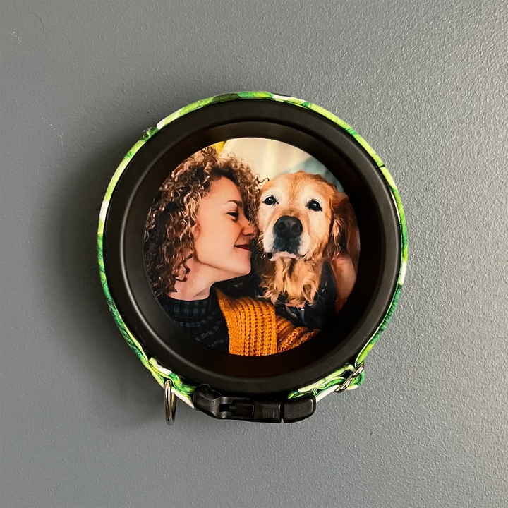 Dog memorial frame with colorful green floral collar displaying a photo of woman and senior Golden Retriever on gray wall