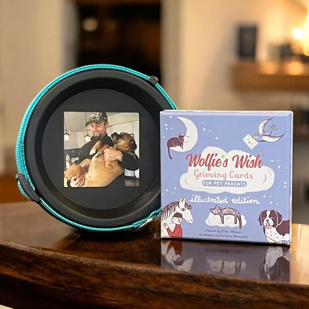 Tribute and Comfort Bundle with a black collar frame showing a man holding his dog and a box of Wolfie’s Wish grieving cards, placed on a dark wooden table.