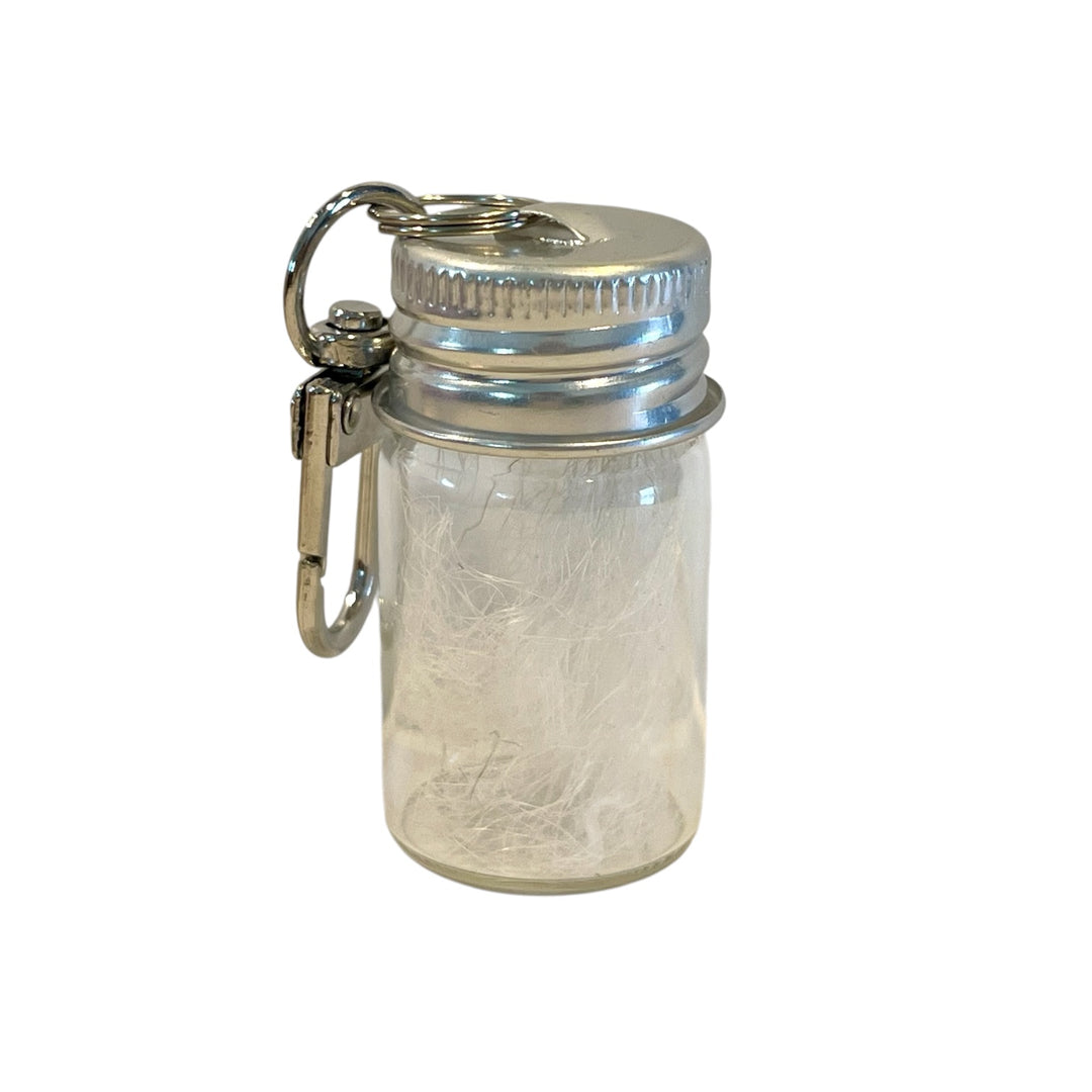 Clear glass jar with metal lid and carabiner on a white background used as a pet fur or ashes keepsake container